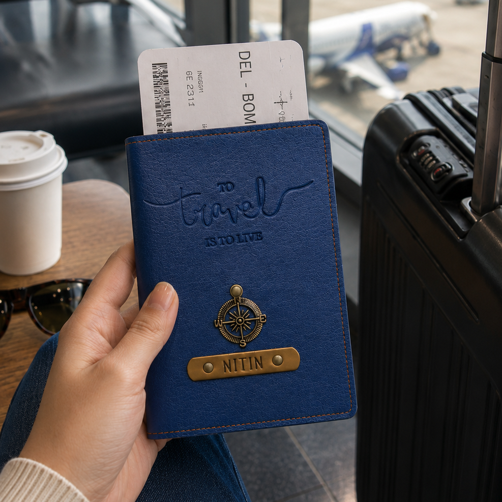 Hand holding a blue travel wallet with passport and tickets, suitcase and coffee cup in background