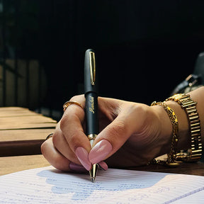 Hand holding a pen with a gold accent, writing on lined paper outdoors.