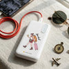 White power bank with a design of a person with a backpack on a textured surface with sunglasses and other items.