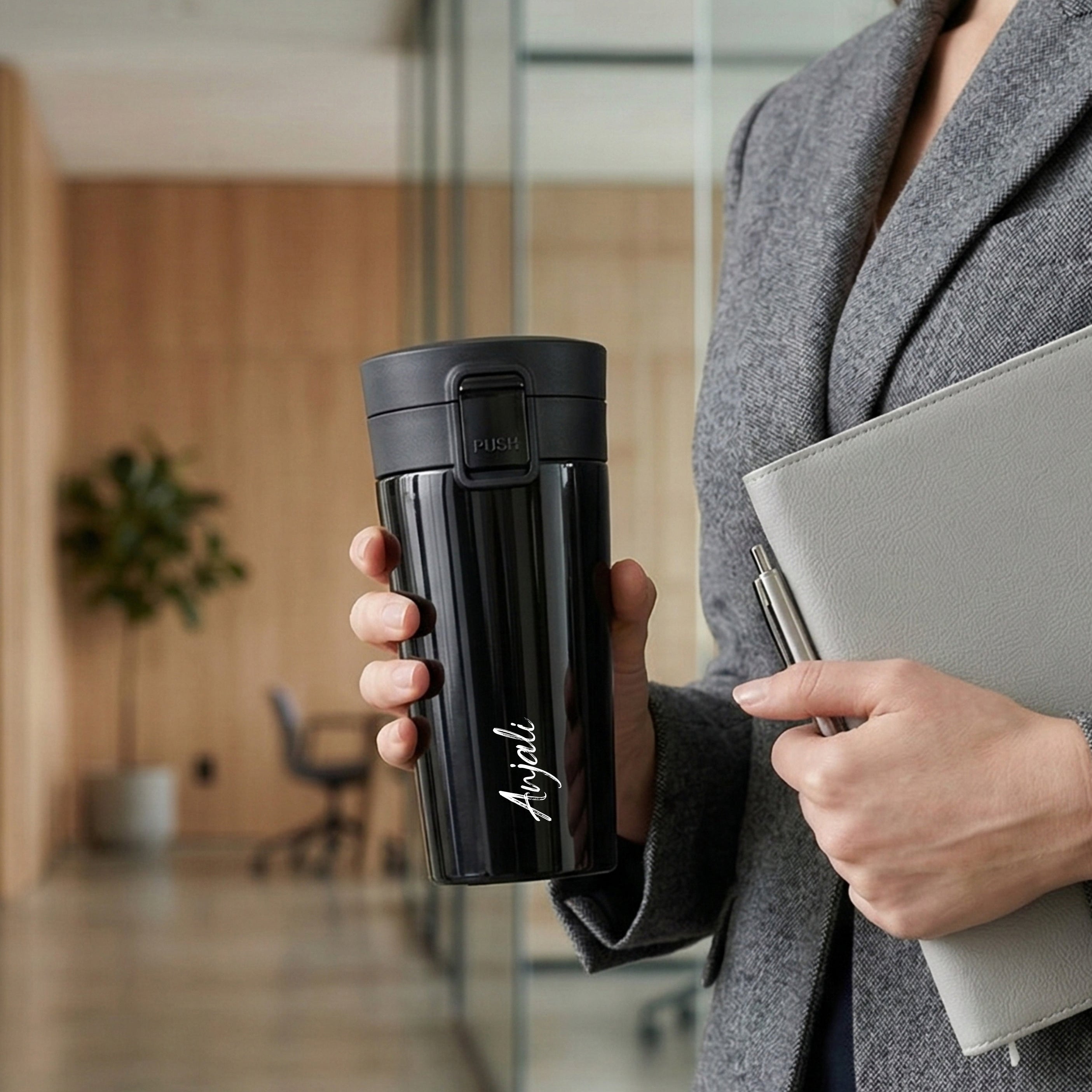 Person holding a black tumbler and a gray notebook in an office setting
